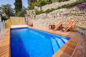 a swimming pool with two chairs and a stone wall at Casa Pomelo, Frigiliana Luxury center townhouse with pool and parking HansOnHoliday Rentals in Frigiliana