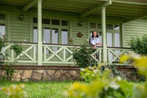 uma mulher sentada num alpendre de uma casa verde em Delta Resort Treetop by Eight Continents em Tulcea