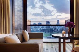 uma sala de estar com um sofá, uma mesa e uma grande janela em Hansar Bangkok Hotel em Banguecoque