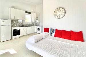 une chambre blanche avec des oreillers rouges et une horloge au mur dans l'établissement Domniki's Sea House, à Asprovalta