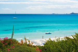 a beach with people and boats in the water at Hotel Simius Playa in Villasimius