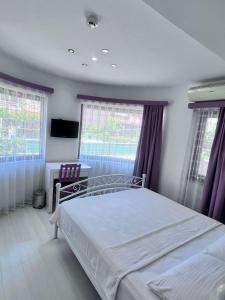 a bedroom with a bed and a desk and windows at Dardanos Pension in Hamidiye