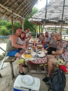un grupo de personas sentadas alrededor de una mesa comiendo comida en BELLA VISTA homestay en Dimbani