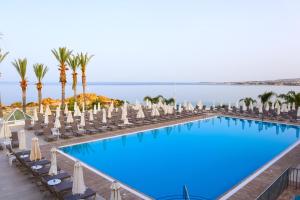 a large swimming pool with chairs and palm trees at Queens Bay Hotel in Paphos