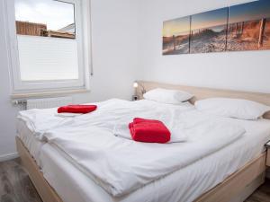 ein weißes Bett mit zwei roten Kissen darauf in der Unterkunft Apartment Ankerweg-2 by Interhome in Norddeich