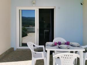 uma mesa branca com cadeiras brancas e uma mesa com copos roxos em Coralie home con piscina e giardino em Lu Razzoni