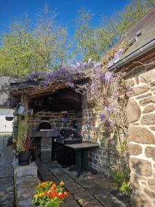 un edificio de piedra con un horno de piedra con flores púrpuras en L'Etang de la Gourdinière, en Landisacq