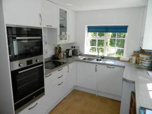 a kitchen with white cabinets and a black appliance at River Cottage a country retreat in wooded gardens in East Stoke