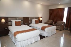 a hotel room with two beds and a chair at The Alcor Hotel in Jamshedpur