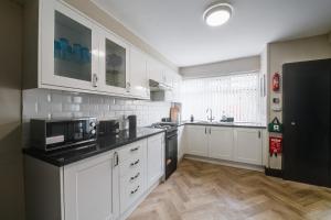 una cocina con armarios blancos y electrodomésticos negros en Poppy's Place - Manningham Road, en Liverpool