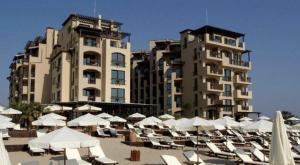 a group of chairs and umbrellas on a beach with buildings at Oazis VIP Club in Sunny Beach
