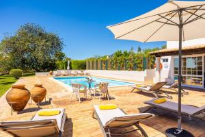 a patio with chairs and an umbrella and a pool at Casa do Carmo in Moncarapacho