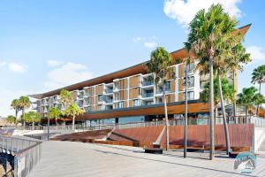 a building with palm trees in front of a boardwalk at Aircabin - Shell Cove - Waterview - 2 Bed Apt in Shellharbour