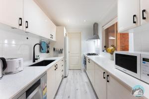 Una cocina blanca con gabinetes blancos y un fregadero. en Aircabin - Seven Hills - Lovely - 3 Beds Townhouse, en Blacktown