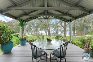 un patio con mesa y sillas en una terraza de madera en Aircabin - Tuggerawong - Waterfront - 4 Beds House, en Karraganbah