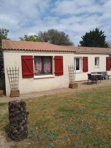 a house with red shutters and a table in a yard at Chambre sous les mimosas 2kms plage in Saint-Jean-de-Monts