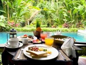 Poka Villa & Spa في أوبود: طاولة مع طبق من المواد الغذائية والمشروبات بجوار حمام السباحة