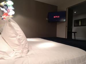 Ein Schlafzimmer mit einem weißen Bett und einem Fernseher an der Wand. in der Unterkunft Hotel le Cinq Hyper - Centre in Chambéry