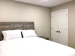 a bedroom with a bed with white sheets and a door at Modern & Luxurious Private Suite in Regina in Regina