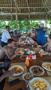 un grupo de personas sentadas alrededor de una mesa comiendo comida en Nightingale Apartments Hotel Mombasa, en Shanzu