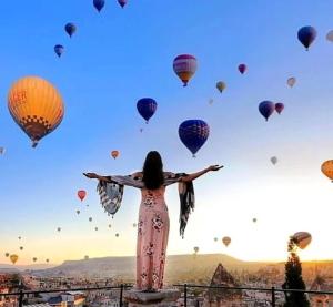 een vrouw op een richel met ballonnen in de lucht bij Very Peri Cappadocia in Uchisar