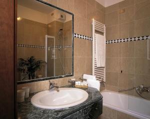 a bathroom with a sink and a mirror and a tub at Hotel De La Ville in Saint Vincent