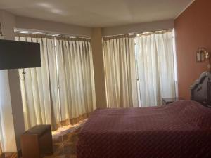 Schlafzimmer mit einem Bett und großen Fenstern mit Vorhängen in der Unterkunft HOTEL ARC&SUITE in Tacna