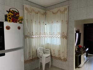 uma cozinha com uma cortina branca, uma cadeira e um frigorífico em Casa Mobiliada Itaubas com ar condicionado em Sinop