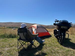 um homem sentado numa cadeira ao lado de uma tenda e uma moto em Infidel Acres Motorcycle Campground em Naches