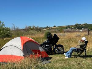 um homem sentado numa cadeira ao lado de uma tenda e uma moto em Infidel Acres Motorcycle Campground em Naches