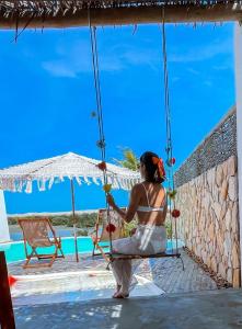 a woman sitting on a swing by a pool at Villakite luxury in Itarema