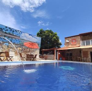 a swimming pool with a red umbrella and a building at Pousada Meu Xodó in São Miguel dos Milagres