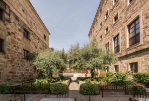 a courtyard with benches and trees between two buildings at Hospes Palacio de San Esteban in Salamanca