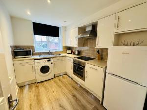 a kitchen with white cabinets and a washer and dryer at West Street Mews - Serviced Accommodation in Exeter