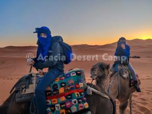 dos personas montando en camello en el desierto en Acacia Desert Camp en Merzouga