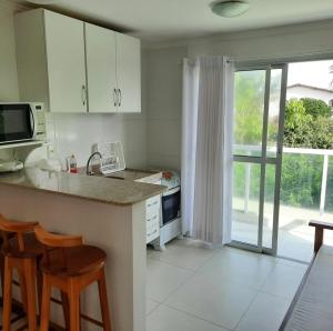 a kitchen with white cabinets and a kitchen island with chairs at Solar de Manguinhos Flat in Manguinhos