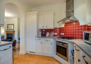 Blythburgh的住宿－Wagtails，厨房配有白色橱柜,墙上铺有红色瓷砖。