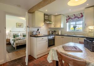 une cuisine avec des placards blancs et une table ainsi qu'une chambre dans l'établissement Gardeners Cottage, à Bealings