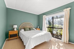 a bedroom with blue walls and a bed with a window at The Wee Bothy - Whangamata Holiday Home in Whangamata