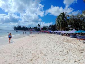 a woman walking on a sandy beach with umbrellas at Steps 2 Beach - 5 Bedroom 3 Bathroom Villa in Christ Church