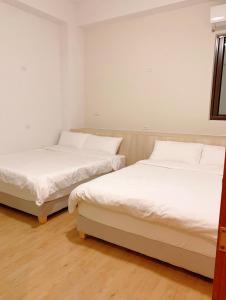 Duas camas num quarto com paredes brancas e pisos em madeira em Travelers Hostel em Magong