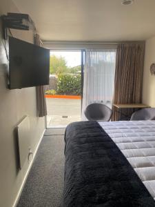 um quarto de hotel com uma cama e uma porta de vidro deslizante em Ashbury Park Motel em Timaru