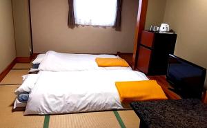 a bedroom with two beds with yellow pillows and a television at ビジネスホテルパークイン石巻 in Inai