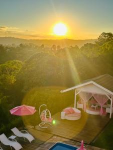 a sunset over a deck with chairs and an umbrella at Pousada Pink Village in Campos do Jordão