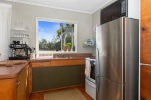 uma cozinha com um frigorífico de aço inoxidável e uma janela em Kereru Cottage - Matapouri Holiday Home em Whangarei