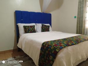 un letto con testiera blu e cuscini sopra di Maridadi place a Kakamega
