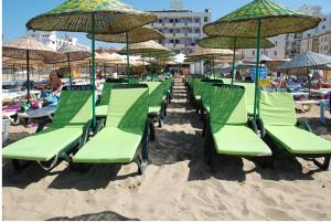 una fila di sedie a sdraio e ombrelloni verdi su una spiaggia di Mostar Hotel a Ayvalık