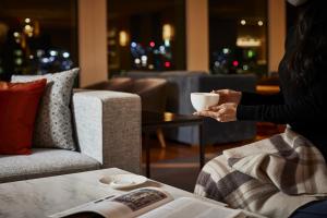 a woman holding a cup of coffee in a living room at Keio Plaza Hotel Tokyo in Tokyo