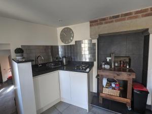 a kitchen with white cabinets and a clock on the wall at Charming 1-Bed Cottage on the outskirts of Haworth in Keighley
