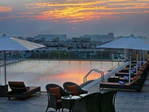 una piscina con sillas, mesas y sombrillas en un edificio en Novotel Pune Viman Nagar Road, en Pune